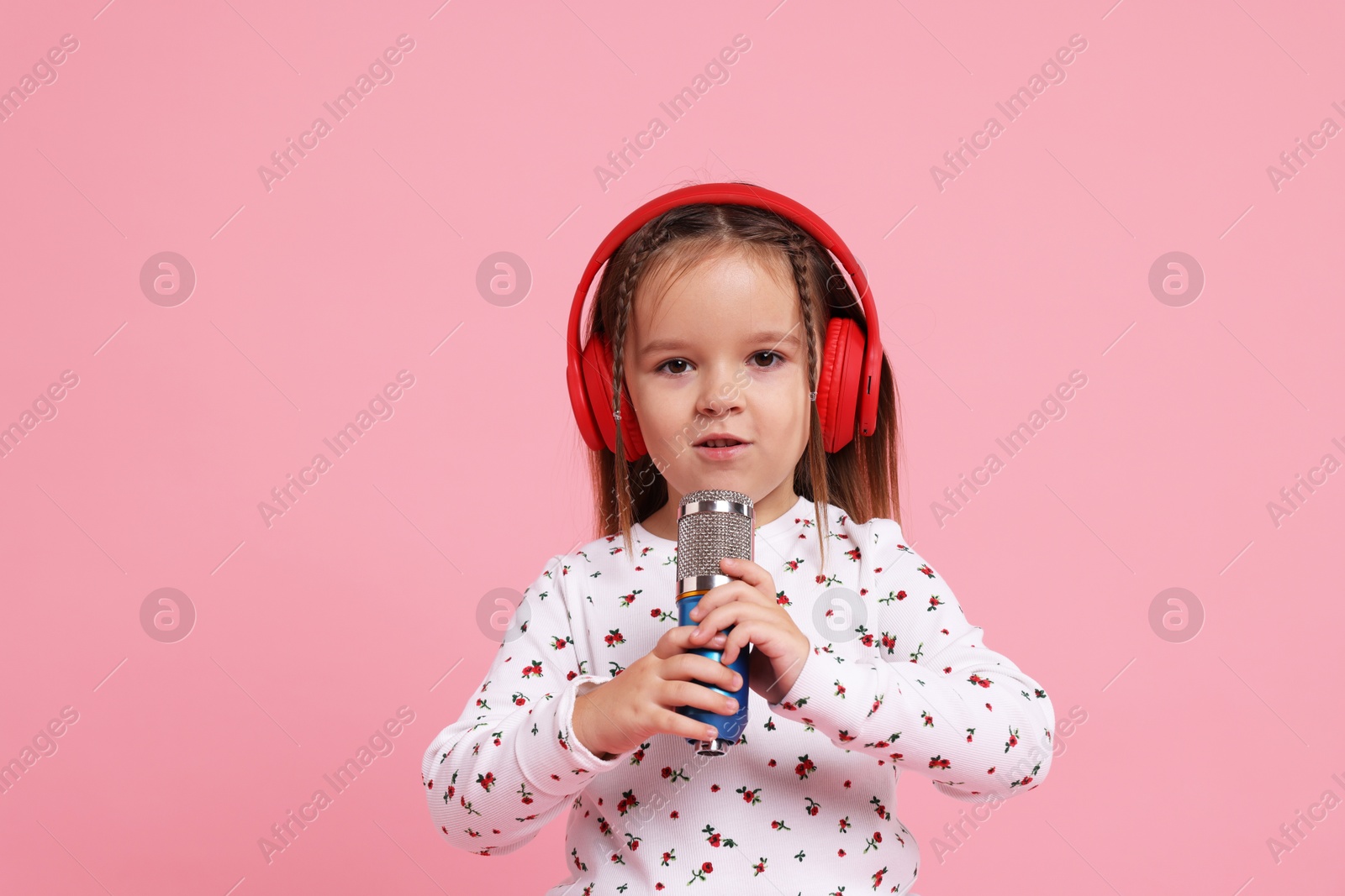 Photo of Cute girl with microphone and headphones singing on pink background