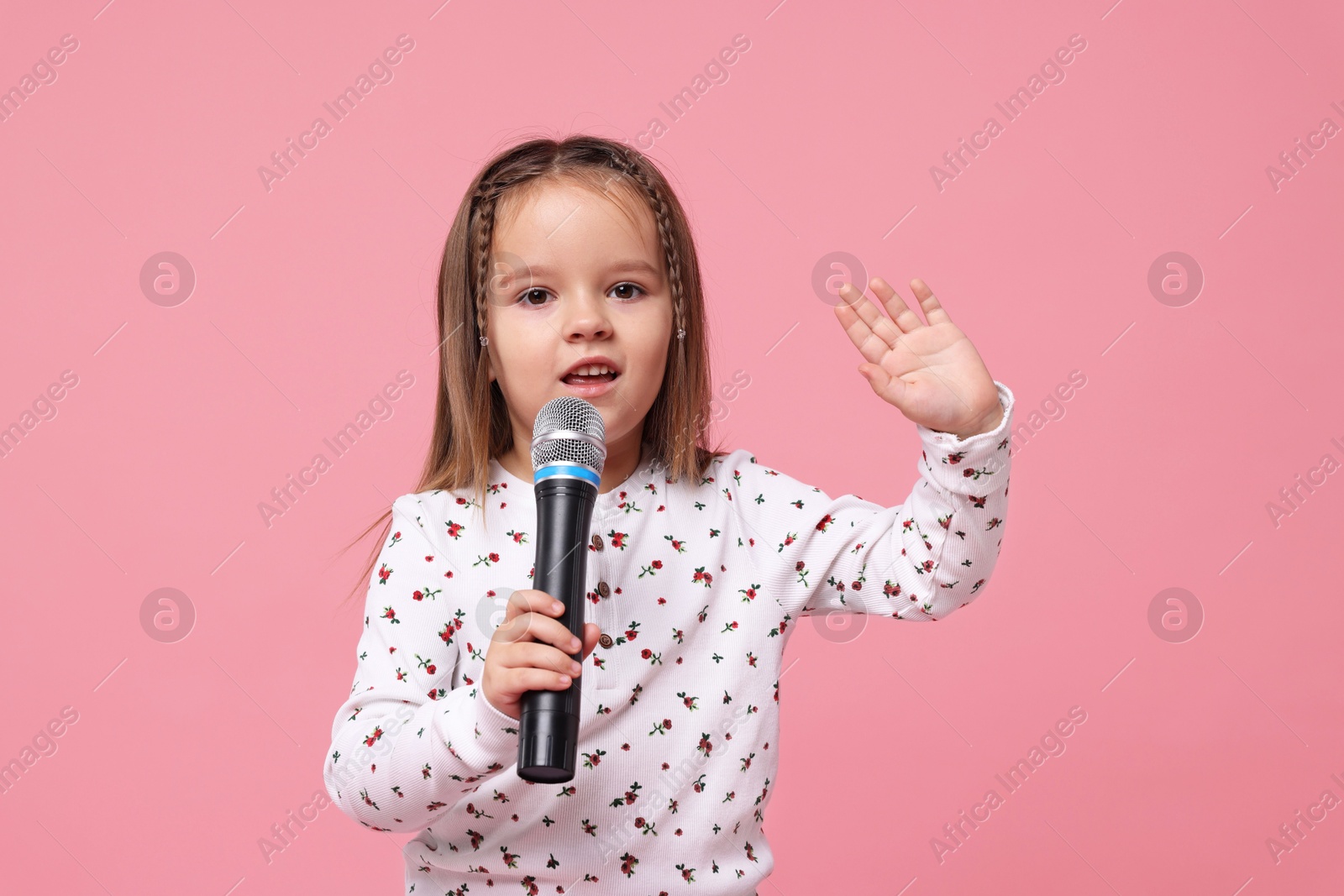 Photo of Cute girl with microphone singing on pink background