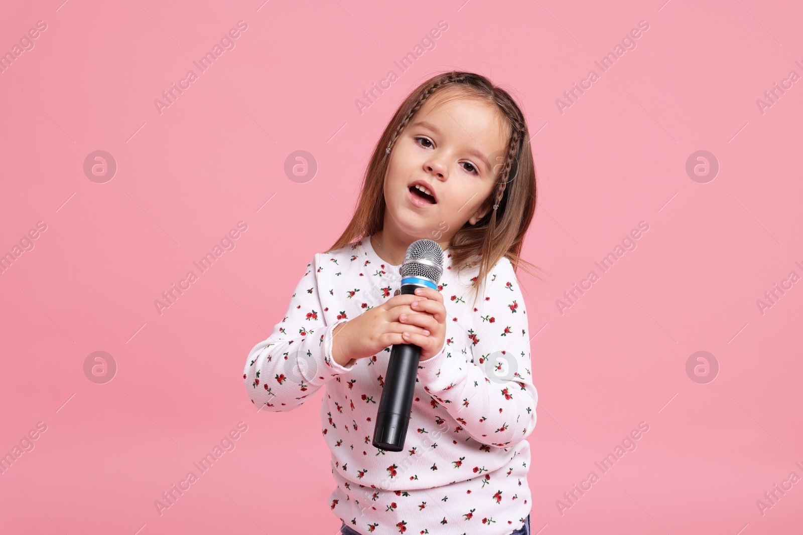 Photo of Cute girl with microphone singing on pink background