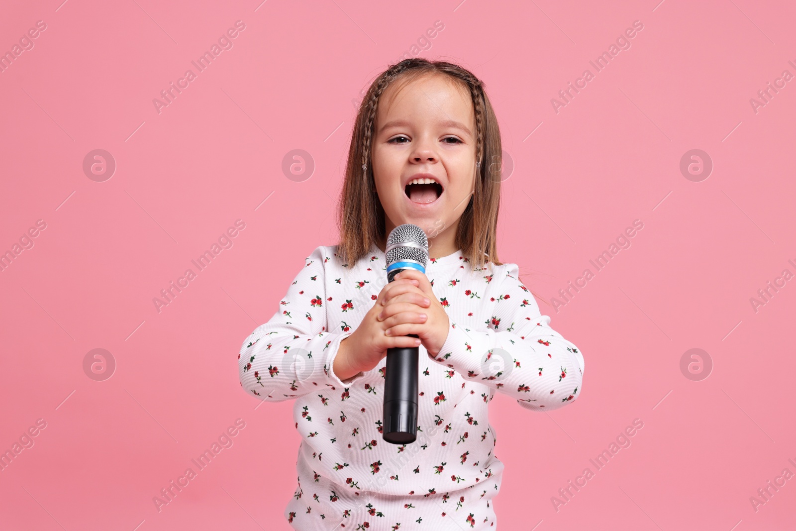 Photo of Cute girl with microphone singing on pink background