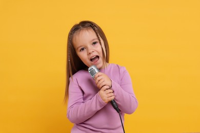 Photo of Cute girl with microphone singing on orange background