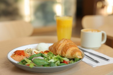 Photo of Tasty breakfast. Freshly baked croissant and salad served on wooden table in cafe, closeup