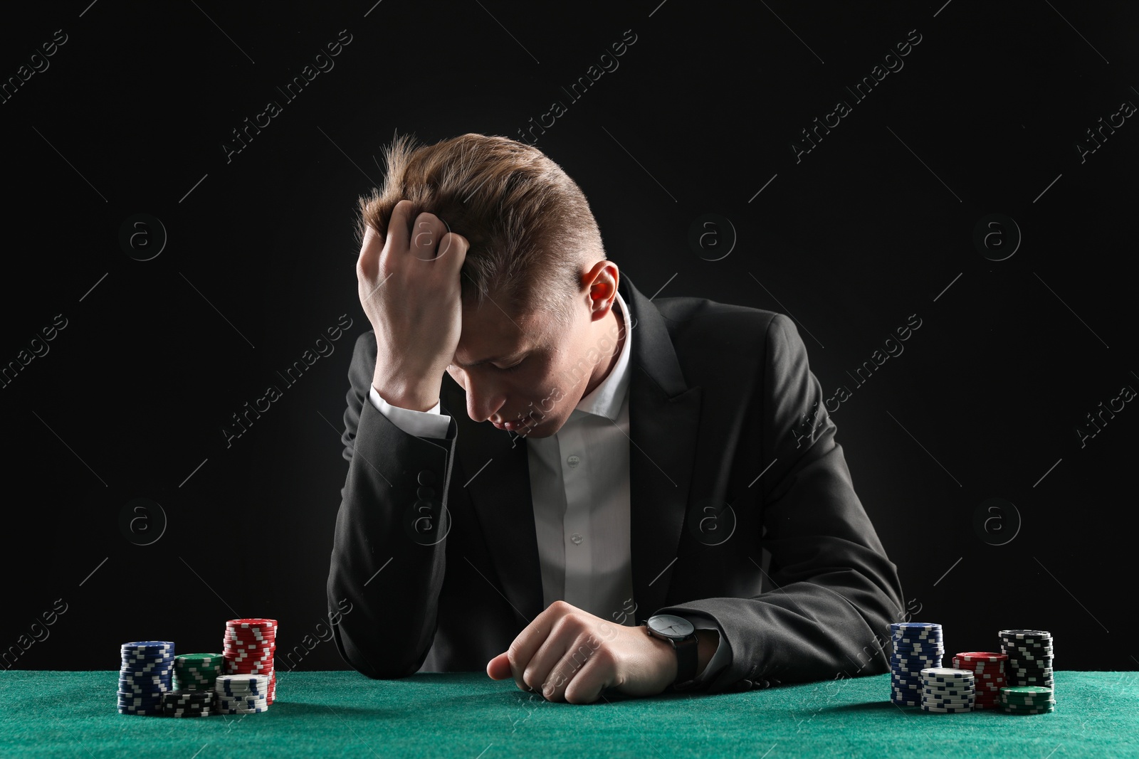 Photo of Sad young man with casino chips at gambling table. Poker concept