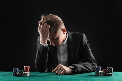 Photo of Sad young man with casino chips at gambling table. Poker concept