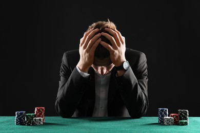 Photo of Sad young man with casino chips at gambling table. Poker concept