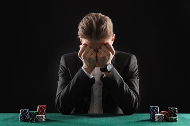 Photo of Sad young man with casino chips at gambling table. Poker concept