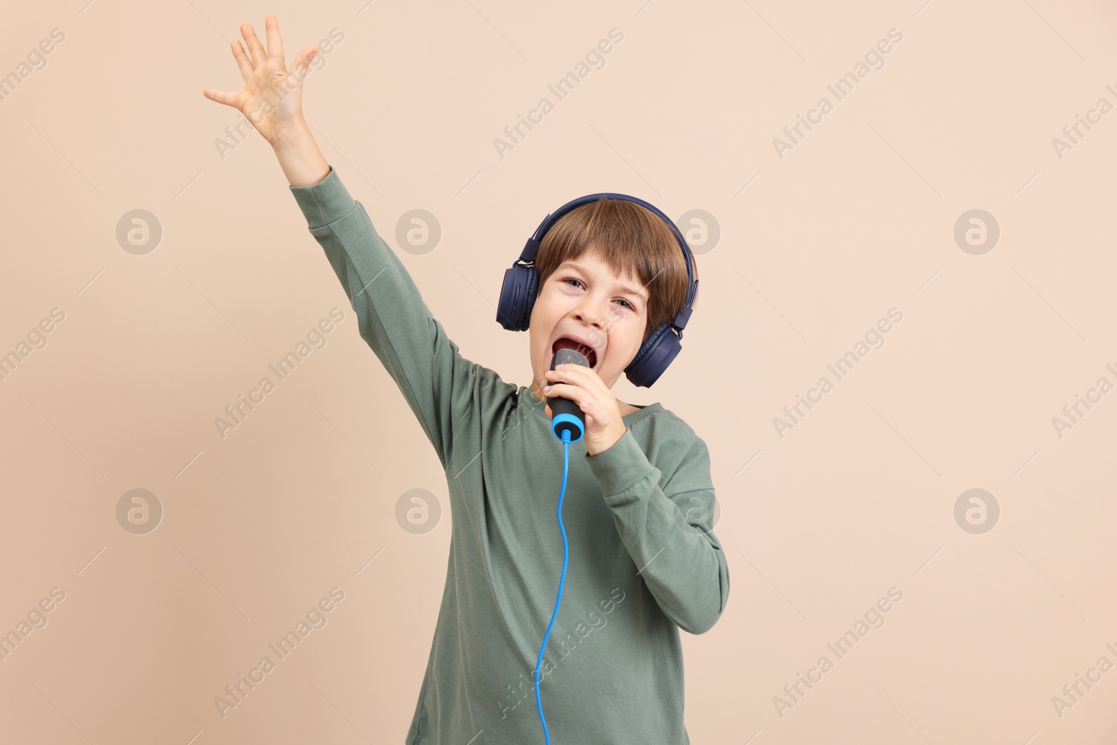 Photo of Cute boy with microphone in headphones singing near beige wall