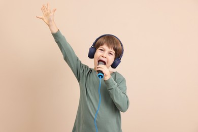 Photo of Cute boy with microphone in headphones singing near beige wall