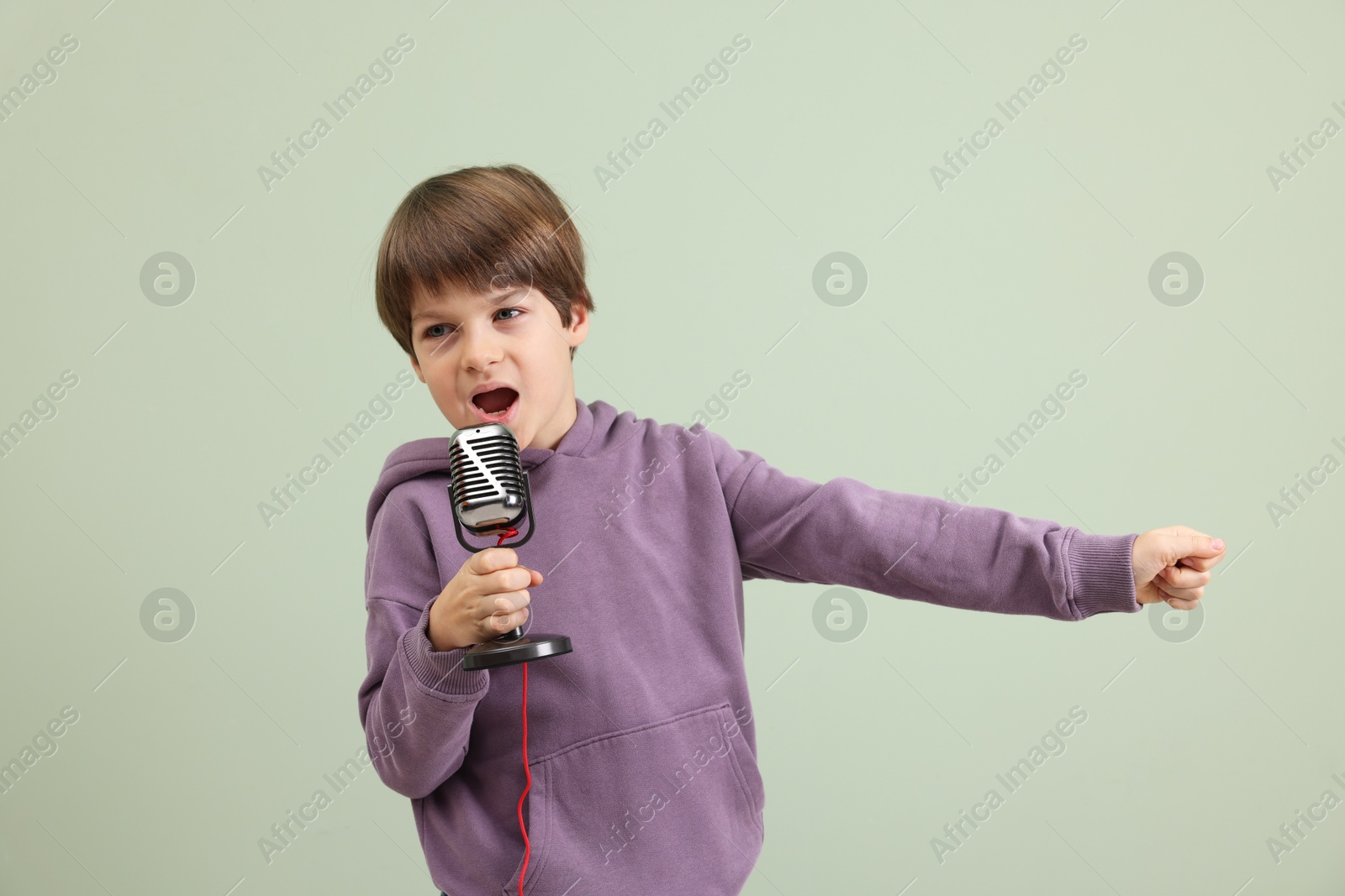 Photo of Cute boy with microphone singing near green wall