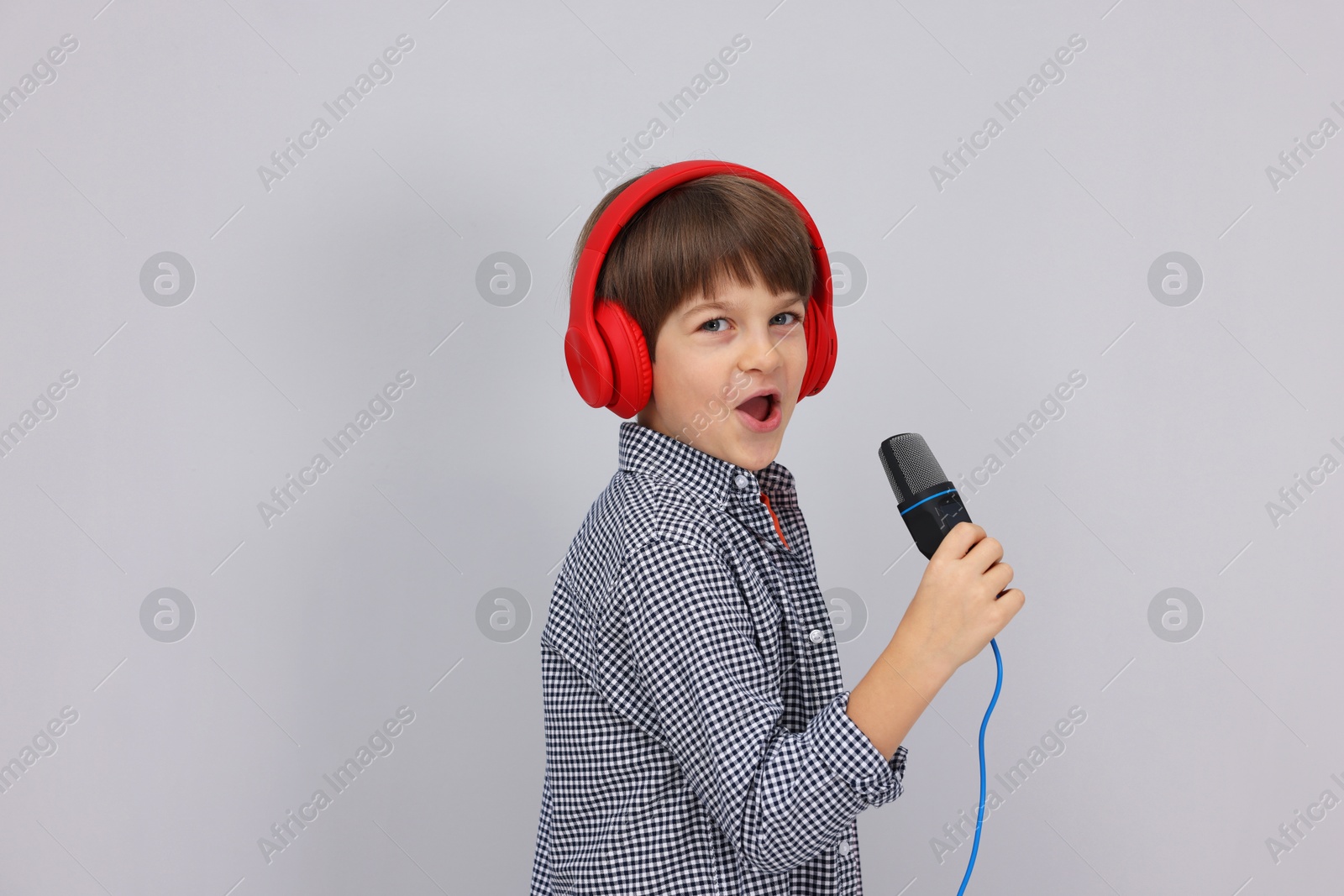 Photo of Cute boy with microphone in headphones singing near grey wall. Space for text