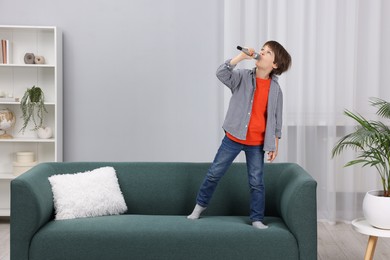 Photo of Cute boy with microphone singing on sofa at home