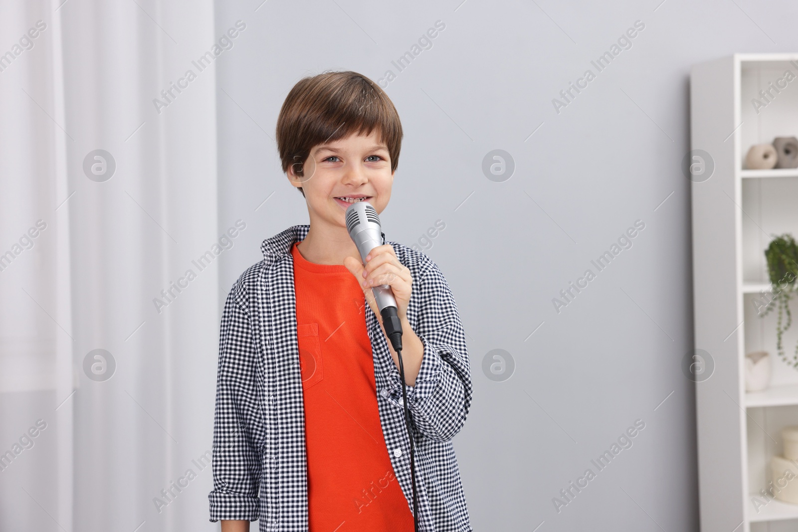 Photo of Cute boy with microphone singing at home. Space for text