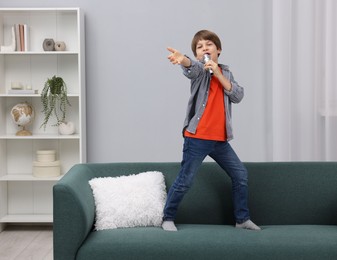 Photo of Cute boy with microphone singing on sofa at home