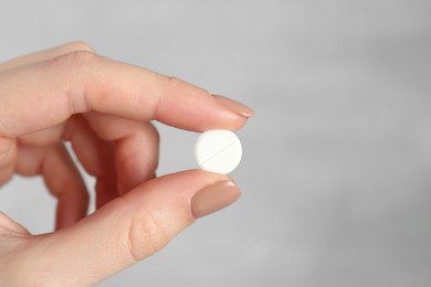 Photo of Woman holding antibiotic pill against grey background, closeup. Space for text