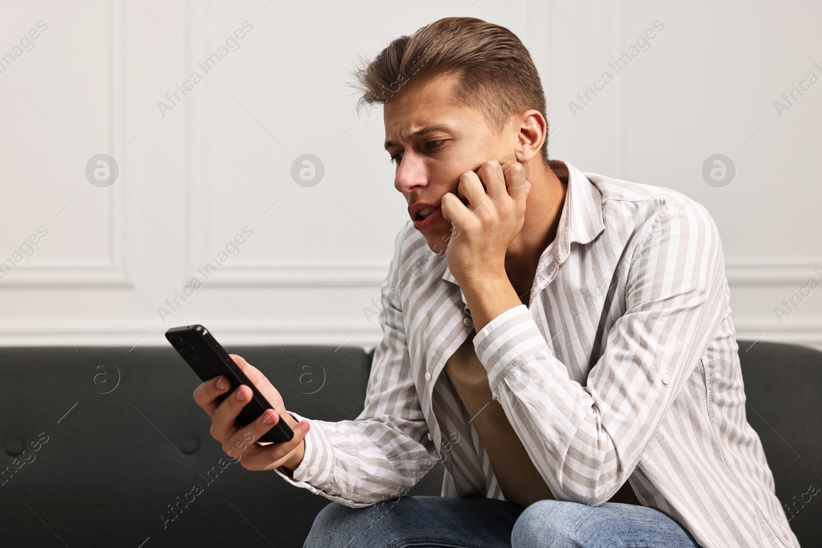 Photo of Worried man calling hotline for mental health help on sofa at home. Space for text