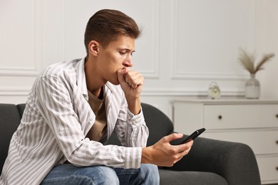 Photo of Worried man calling hotline for mental health help on sofa at home. Space for text