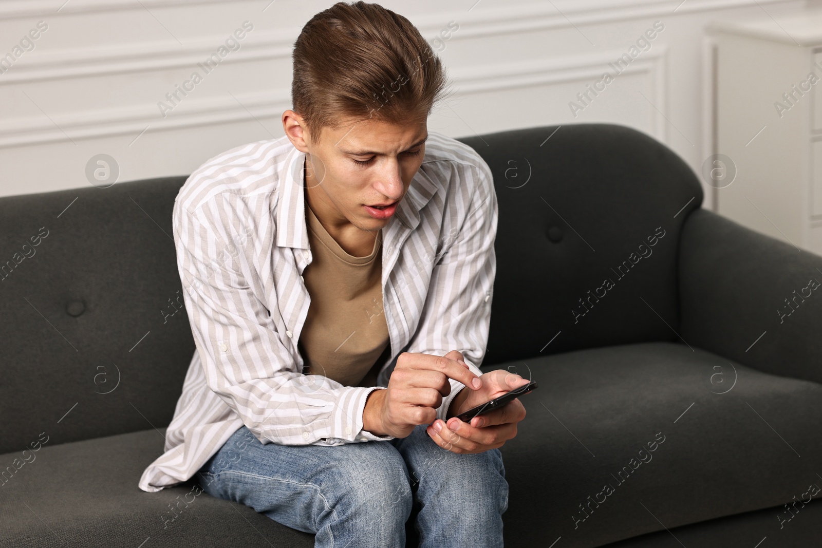 Photo of Worried man calling hotline for mental health help on sofa at home