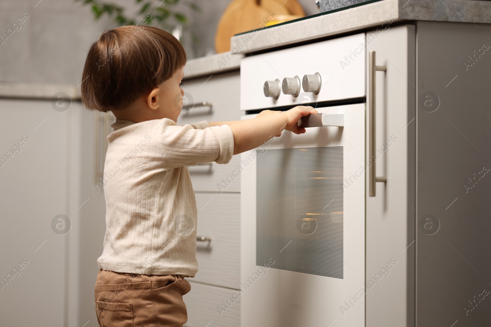 Photo of Little boy playing with oven in kitchen. Dangerous situation