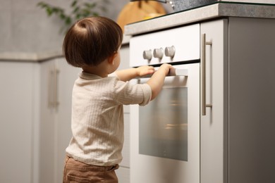 Photo of Little boy playing with oven in kitchen. Dangerous situation