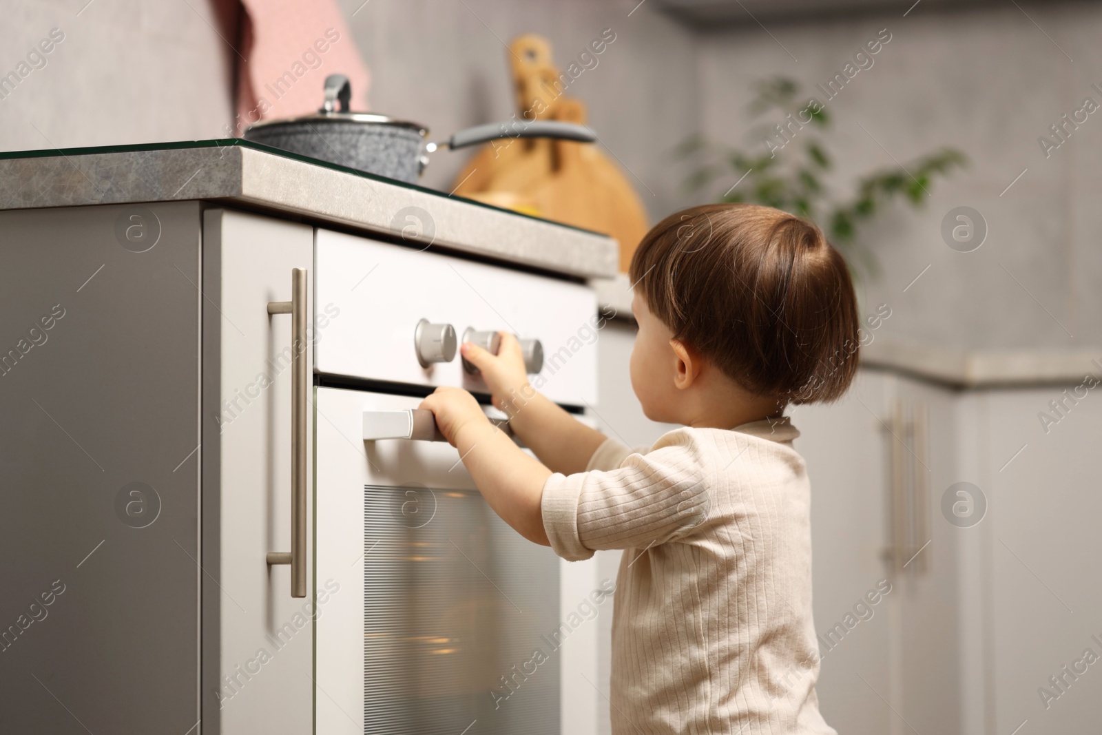 Photo of Little boy playing with oven in kitchen. Dangerous situation