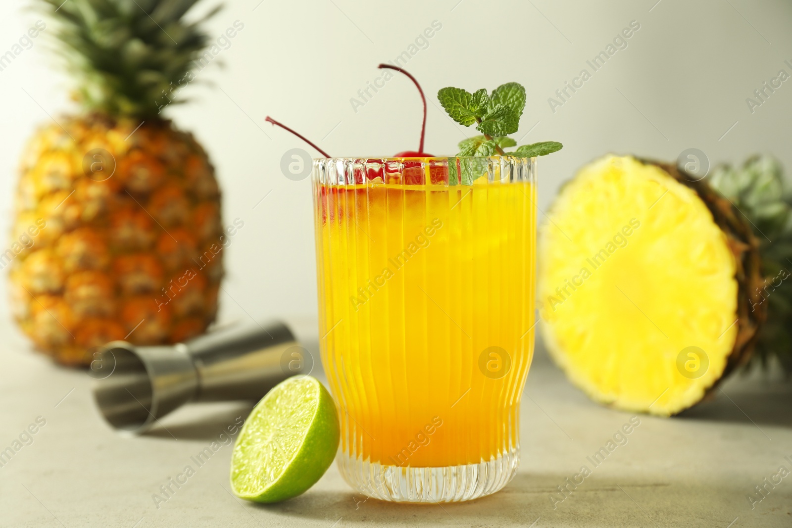 Photo of Tasty pineapple cocktail with mint and cherry in glass served on light table, closeup