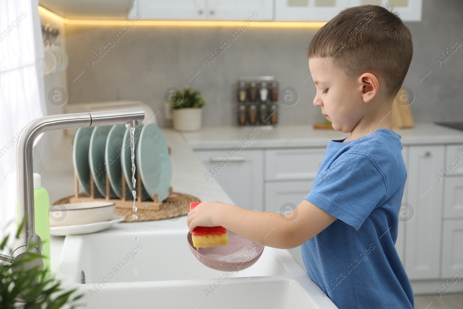 Photo of Little helper. Cute boy washing dishes at home