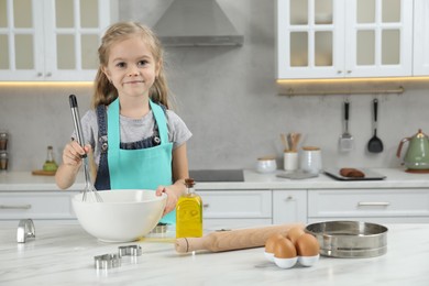 Photo of Little helper. Cute girl making dough for cookies in kitchen at home, space for text