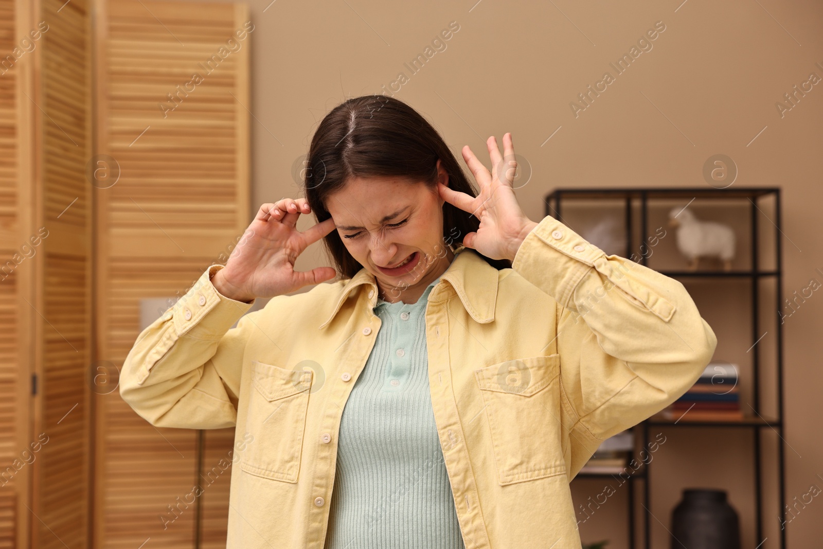 Photo of Annoyed woman covering her ears due to loud sound at home