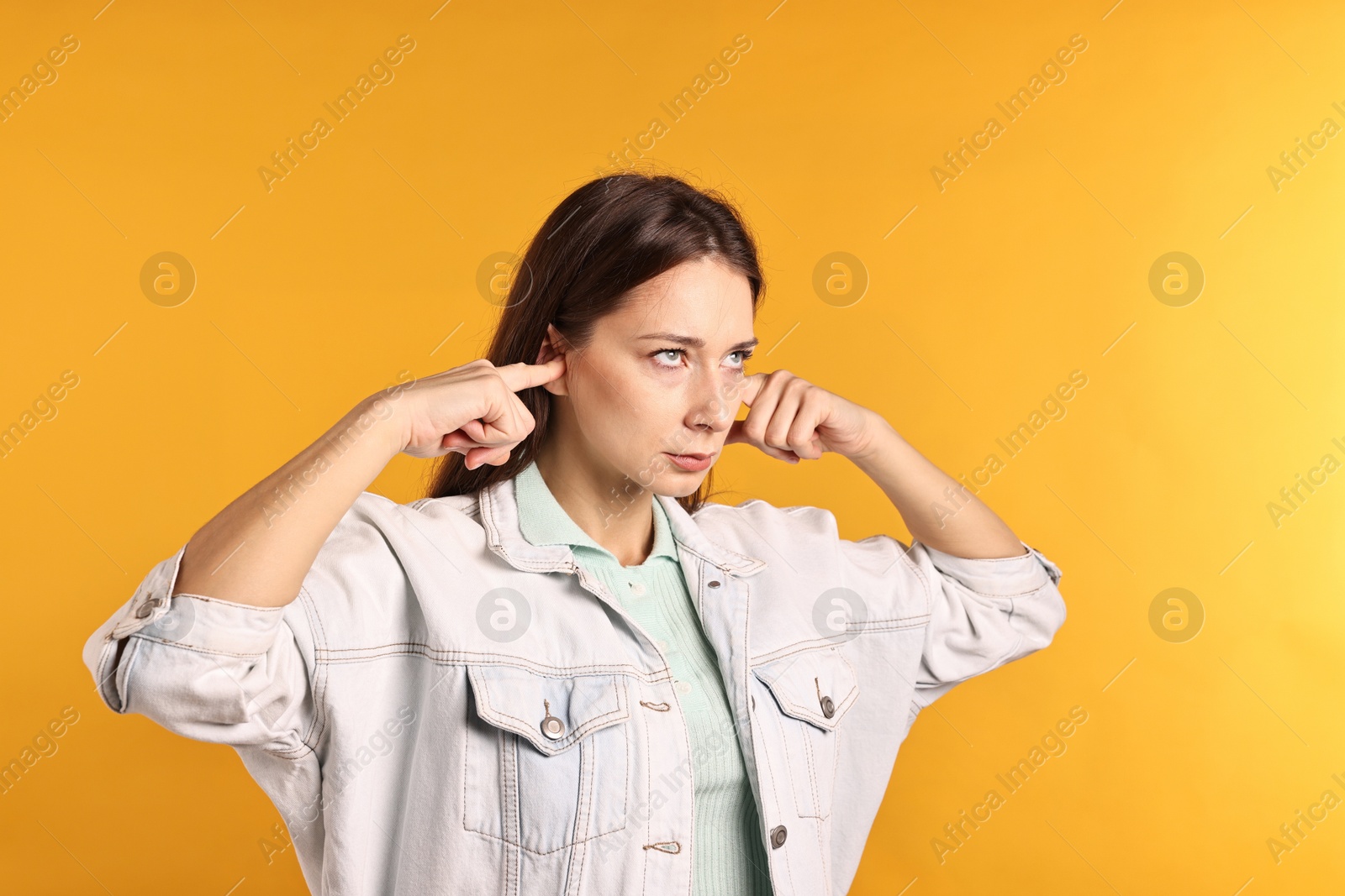 Photo of Annoyed woman covering her ears due to loud sound on orange background