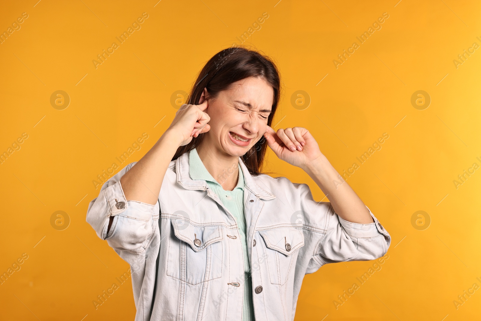 Photo of Annoyed woman covering her ears due to loud sound on orange background