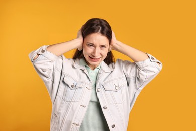 Photo of Annoyed woman covering her ears due to loud sound on orange background