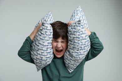 Photo of Annoyed boy covering his ears with pillows due to loud sound on grey background