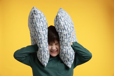 Photo of Annoyed boy covering his ears with pillows due to loud sound on yellow background