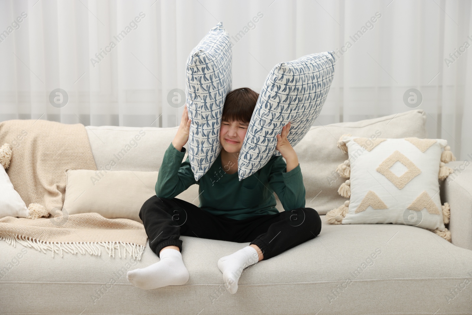 Photo of Annoyed boy covering his ears due to loud sound on sofa at home