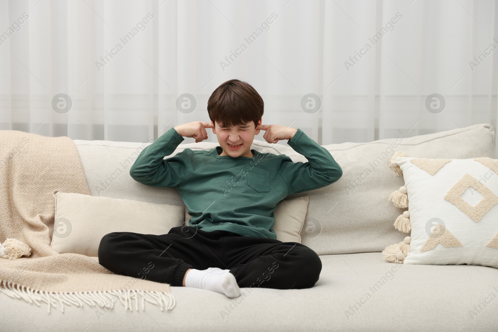 Photo of Annoyed boy covering his ears due to loud sound on sofa at home