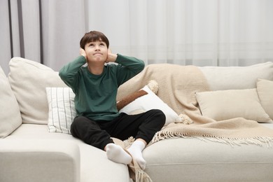 Photo of Annoyed boy covering his ears due to loud sound on sofa at home, space for text