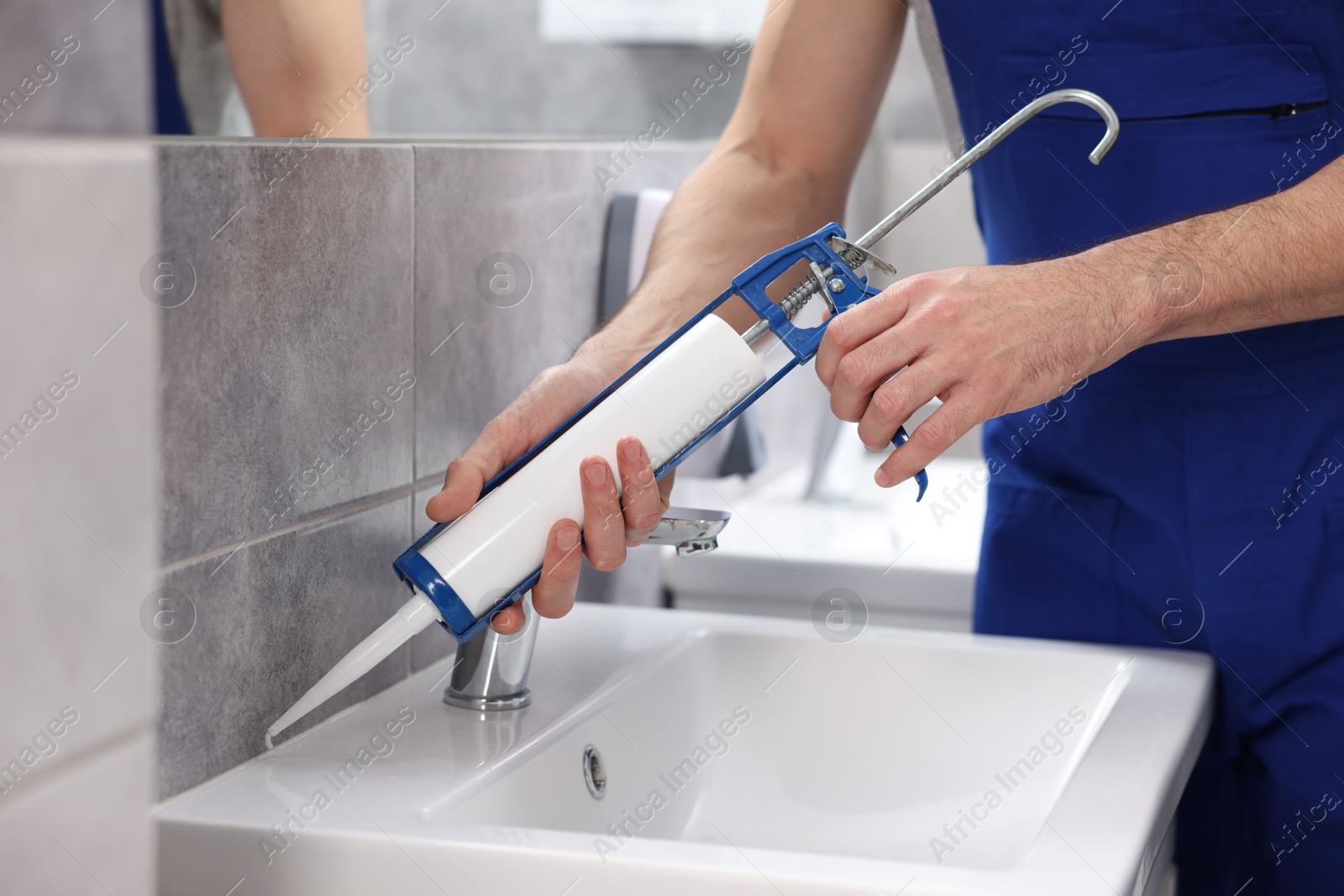 Photo of Worker with caulking gun sealing washbasin in bathroom, closeup