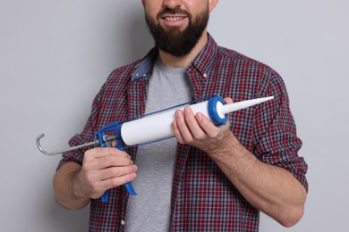 Photo of Man with caulking gun on gray background, closeup