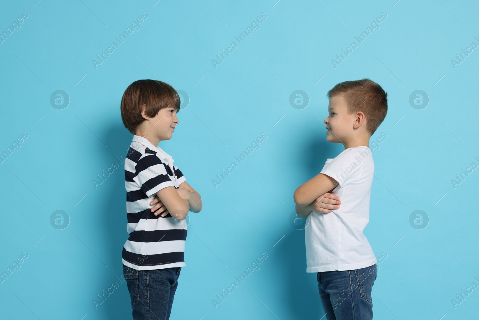 Photo of Brothers with crossed arms arguing on light blue background