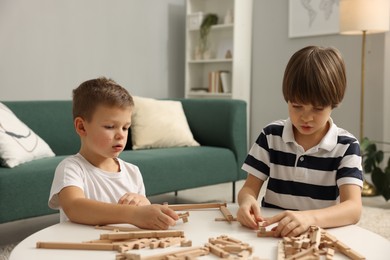 Photo of Cute brothers playing with wooden construction set at table indoors