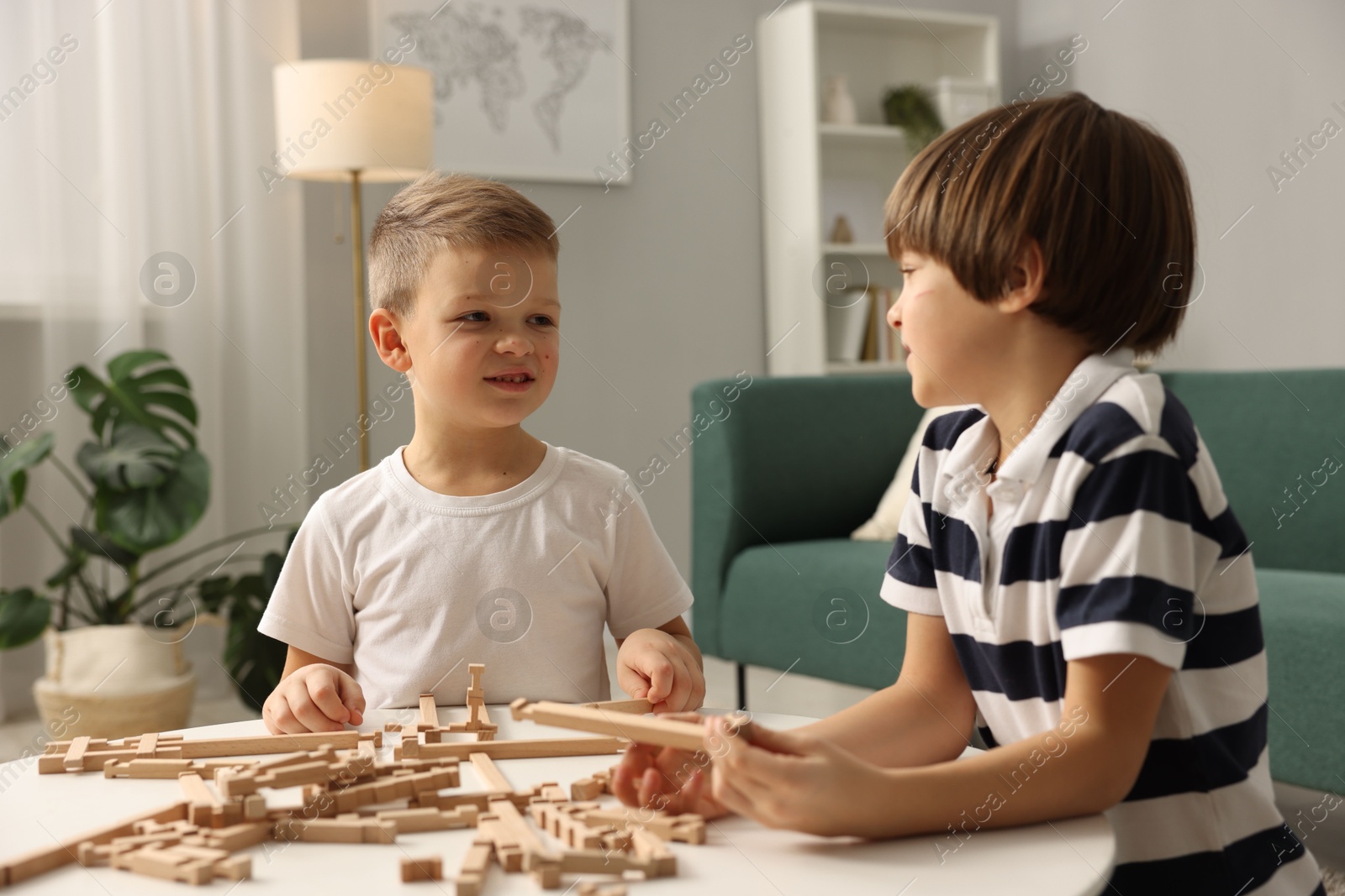 Photo of Cute brothers playing with wooden construction set at table indoors