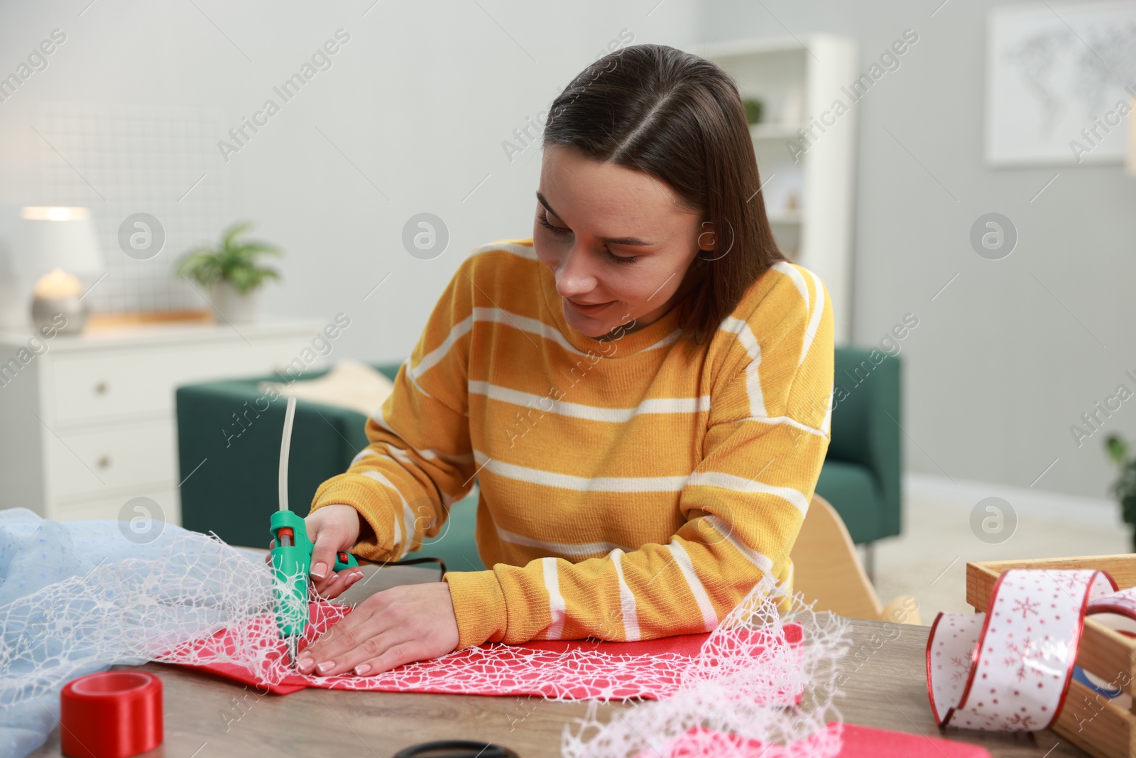 Photo of Woman with hot glue gun making craft at table indoors