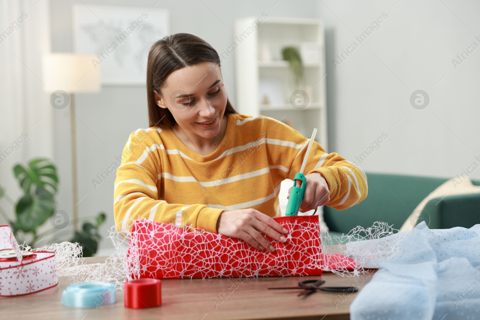 Photo of Woman with hot glue gun making craft at table indoors