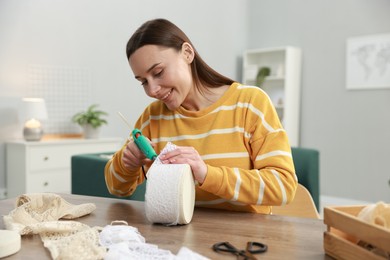 Woman with hot glue gun making craft at table indoors