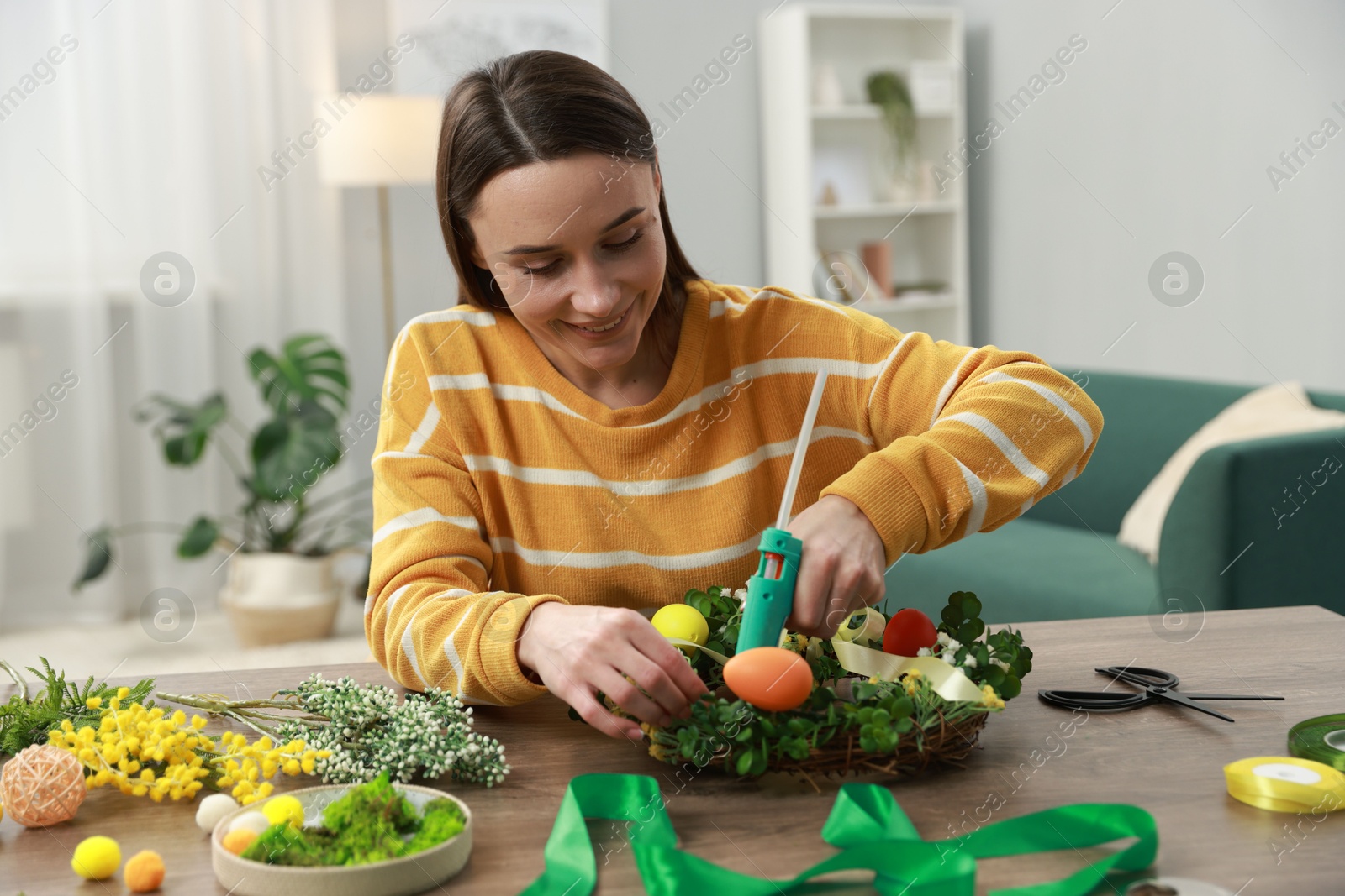 Photo of Woman with hot glue gun making craft at table indoors