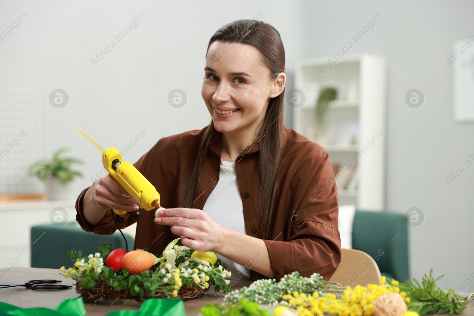 Photo of Woman with hot glue gun making craft at table indoors