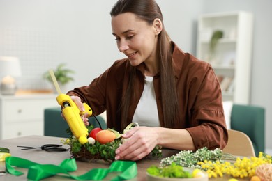 Photo of Woman with hot glue gun making craft at table indoors