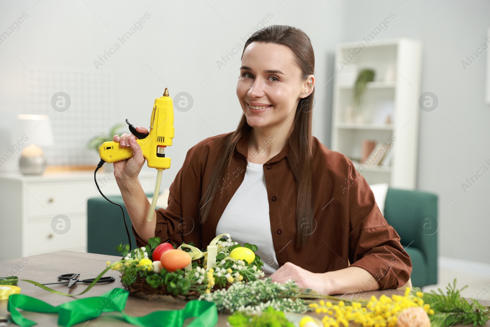 Photo of Woman with hot glue gun at table indoors