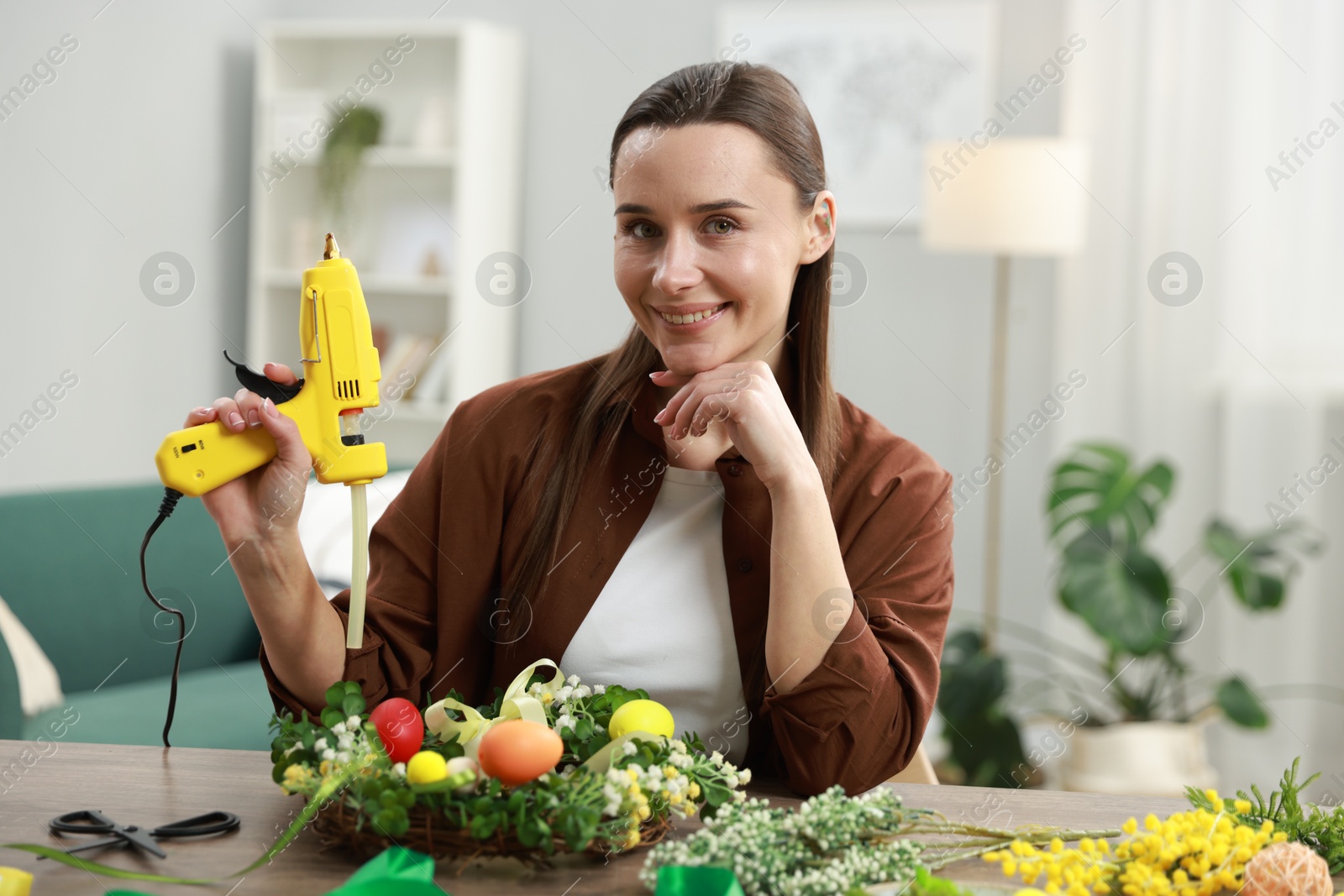 Photo of Woman with hot glue gun at table indoors