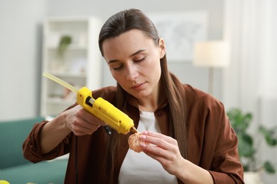 Photo of Woman with hot glue gun making craft at table indoors